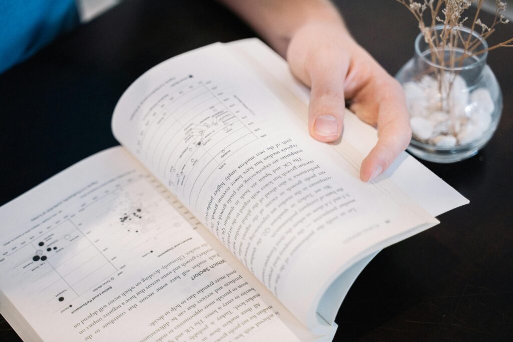 An open book being held by a young man sitting at a desk at home.