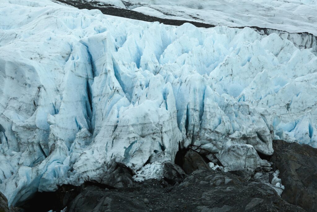 The edge of a small glacier field with black rocks in the foreground.